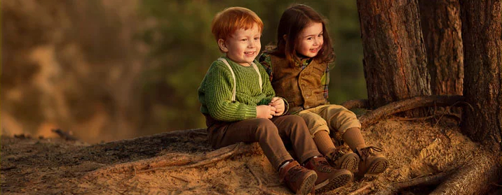 Zwei Kinder sitzen entspannt in einem natürlichen Waldumfeld – Sinnbild für umweltverträgliche Baumaterialien und gesundes Wohnklima durch nachhaltige Dämmstoffe.